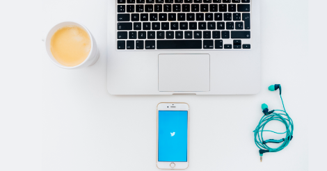 Laptop on desk, with smartphone featuring Twitter on the screen and a cup of coffee next to it.